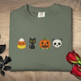 Folded gray t-shirt with Halloween designs, featuring a candy corn, black cat, pumpkin, and skull. Black and red roses lie beside it on a wooden surface.