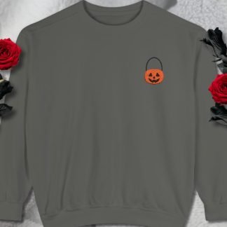 Gray sweatshirt with a small, orange Jack-o'-lantern embroidery on the left chest. Surrounded by two red roses on a soft, fluffy white background. Cozy and festive mood.