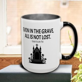 A white mug with a black handle on a windowsill, featuring a tombstone design and an Edgar Allan Poe quote, "Even in the grave, all is not lost."