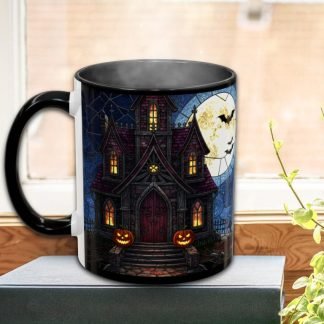 A black mug on a windowsill depicts a haunted house with glowing pumpkins, a full moon, and flying bats, conveying a spooky Halloween theme.