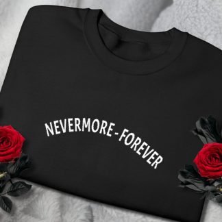 Folded black sweatshirt with "NEVERMORE-FOREVER" in white text. Two vivid red roses frame the sweatshirt on a soft, light gray fabric background.