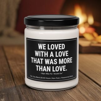 A white candle in a glass jar with a black lid sits on a wooden table. The label reads, "We loved with a love that was more than love." A cozy fireplace glows softly in the background.