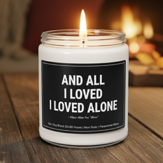 A white candle in a glass jar with a black lid on a wooden surface. The label quotes Edgar Allan Poe: "And all I loved, I loved alone." A cozy, lit fireplace is blurred in the background, conveying warmth and introspection.